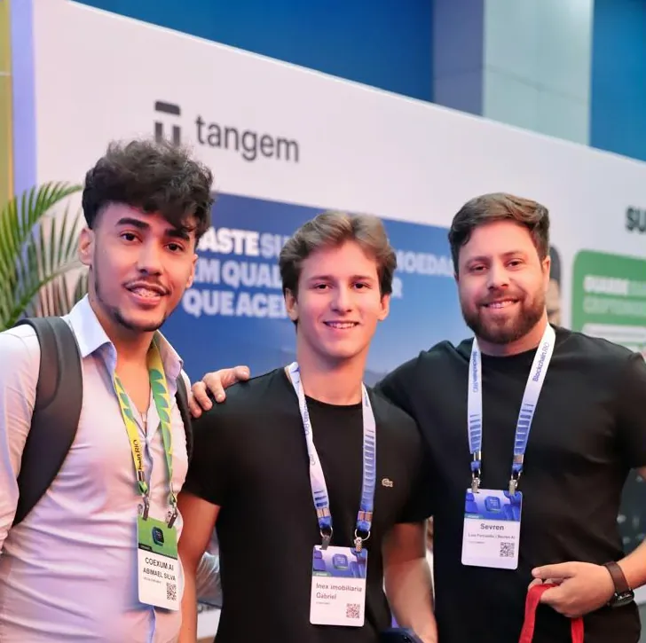 Abimael com dois participantes do evento diante de um estande